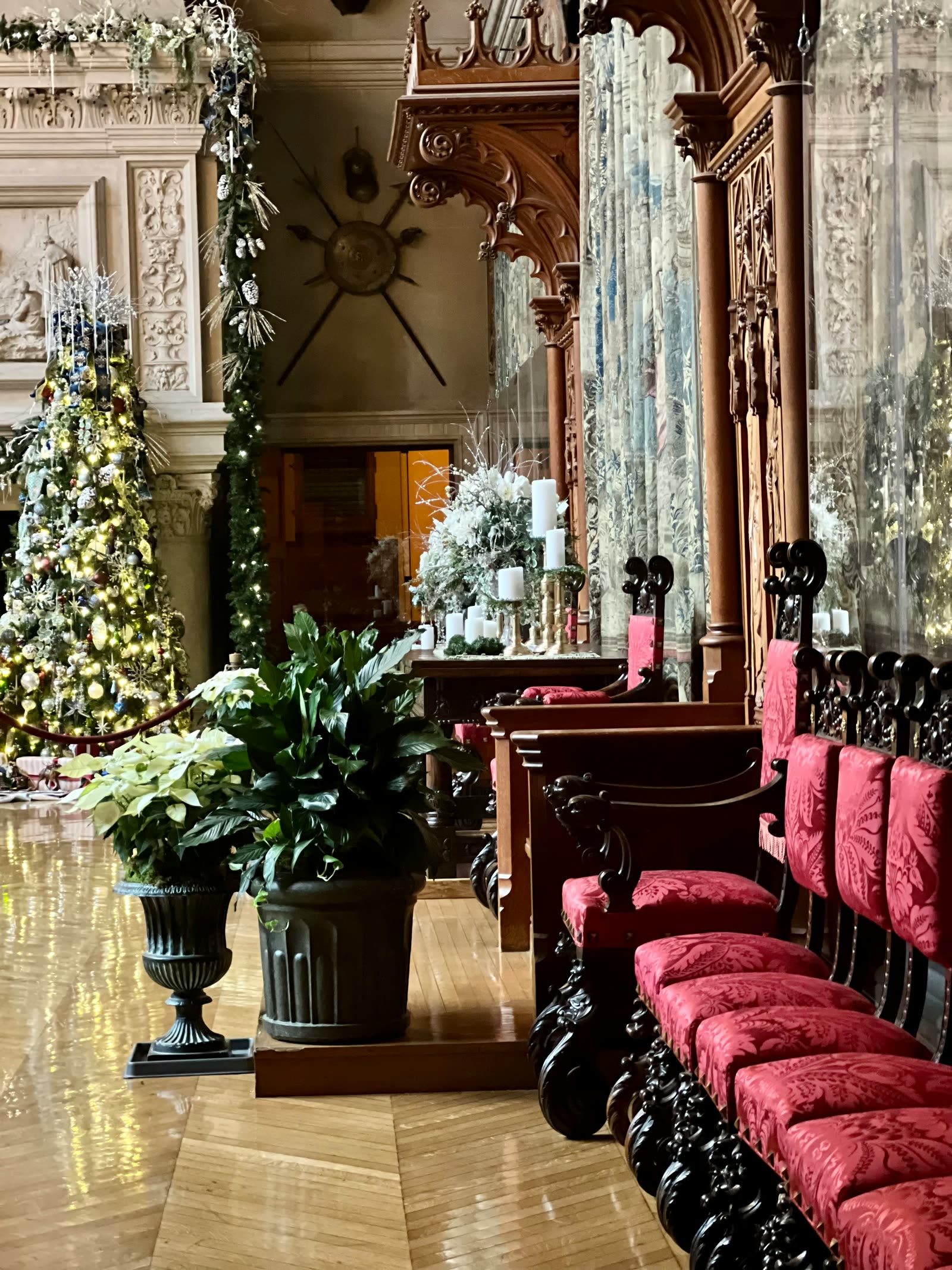 The Banquet Hall at Biltmore House decorated for Christmas, with a tall lit tree beside the triple fireplace