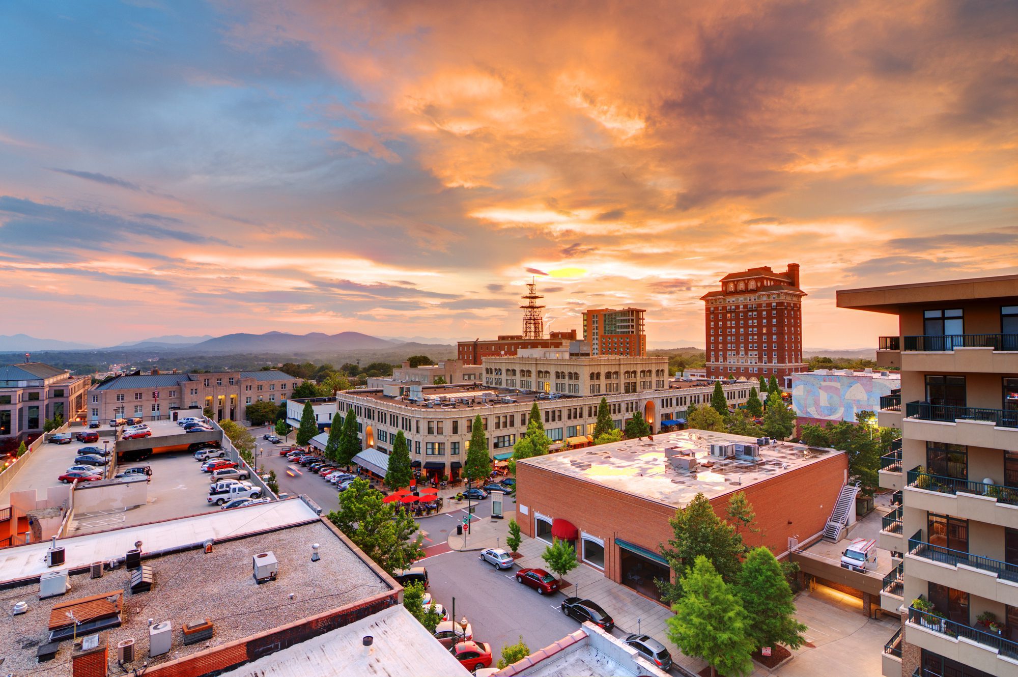The Asheville skyline in summer: towers rising over green trees under a blue sky with high clouds