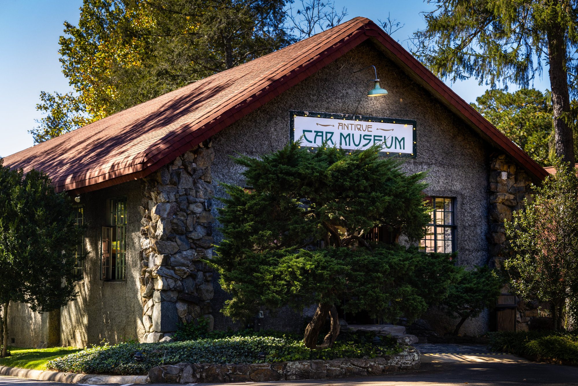 A stone gable lettered &ldquo;Antique Car Museum&rdquo; in green art-nouveau capitals, strung with lights.