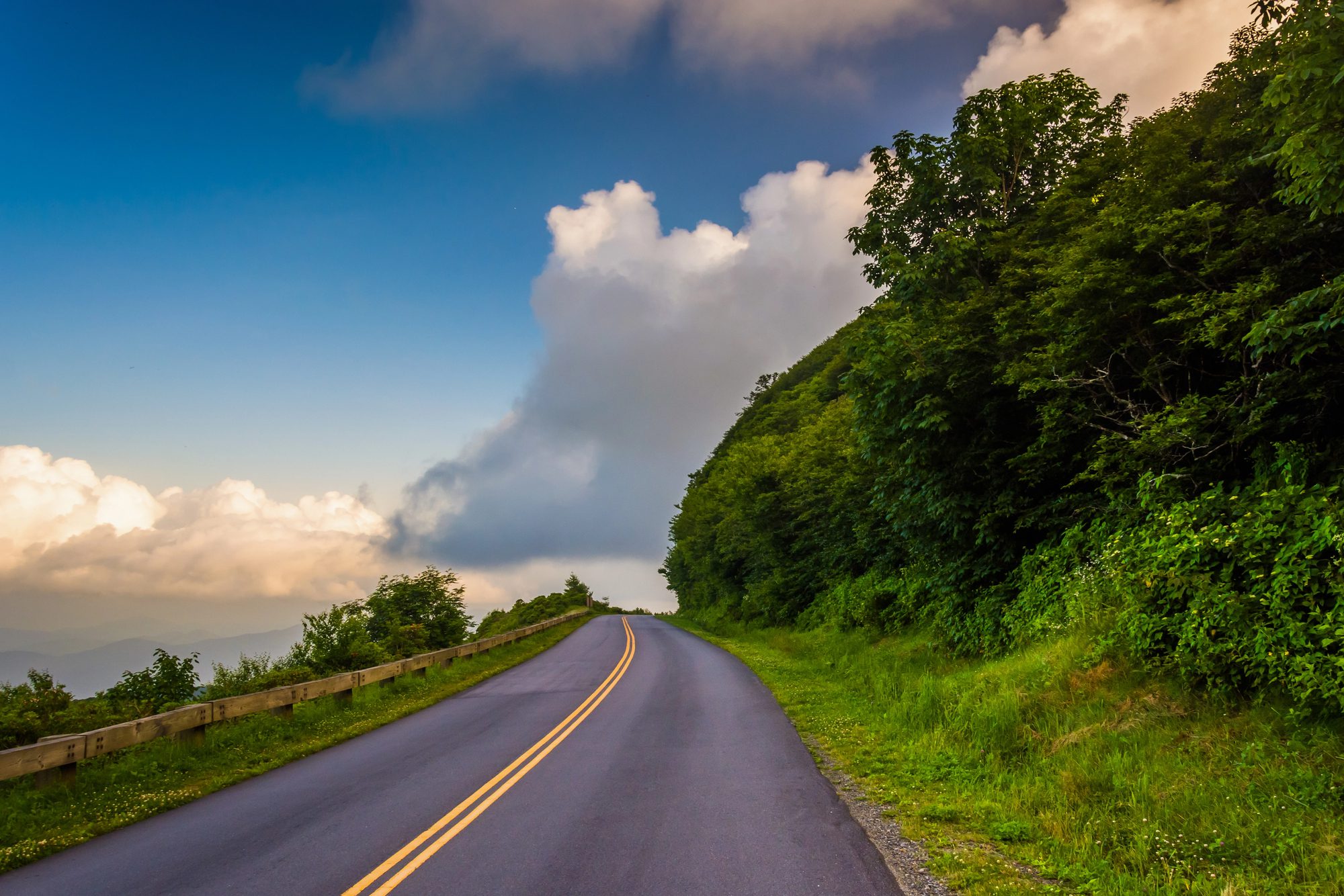 Two-lane parkway road running along a wooded ridge, with a valley opening out beyond the trees