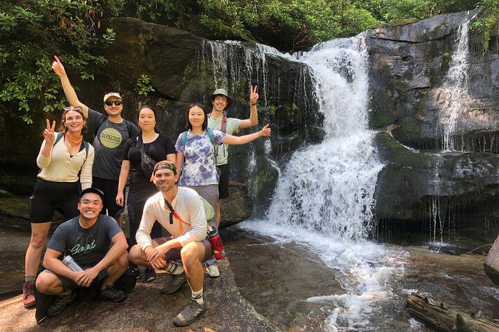 A group of guests posing at the foot of a wide, rock-ledge waterfall in summer