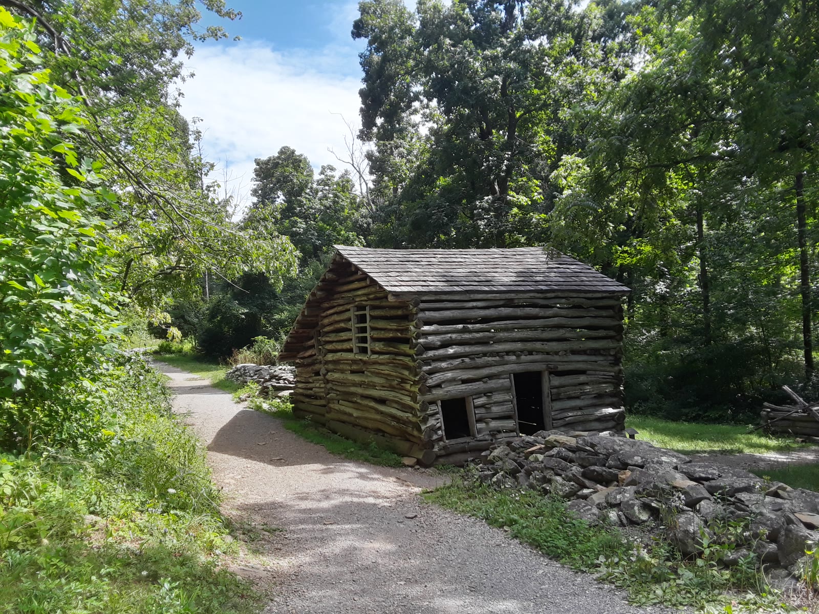 Humpback Rocks, VA. Grey chestnut-log farm buildings with split-rail fencing on an open hillside; hikers on a bare rock ledge above a hazy valley.