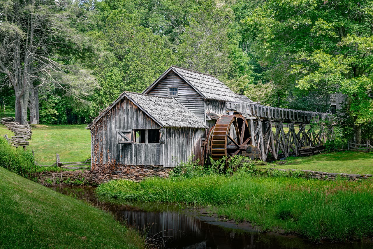 Mabry Mill, VA. A dark weathered board mill with an overshot wooden water wheel mirrored in the still millpond in front of it.