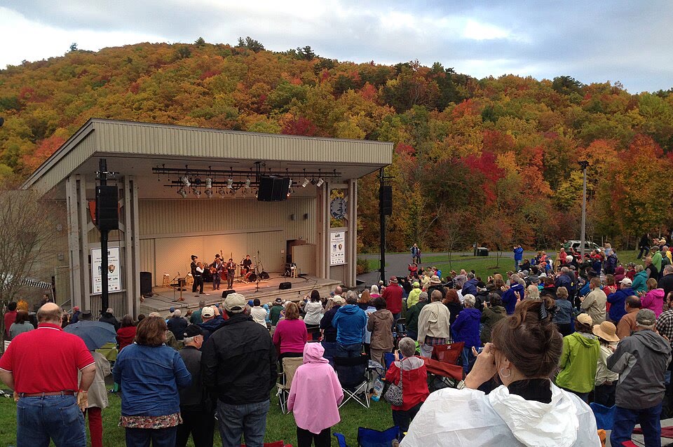 Blue Ridge Music Center, VA. A grass-bowl amphitheater with mountain ridgelines directly behind the stage; musicians playing in the open breezeway.