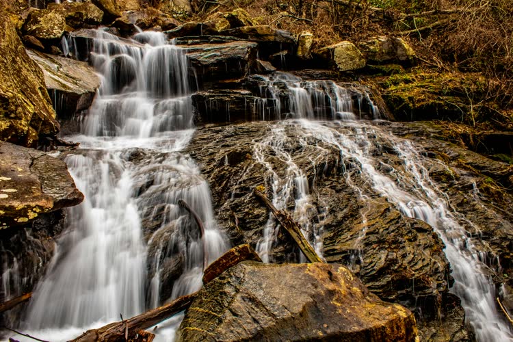 A white ribbon of waterfall dropping through dark rock and green forest